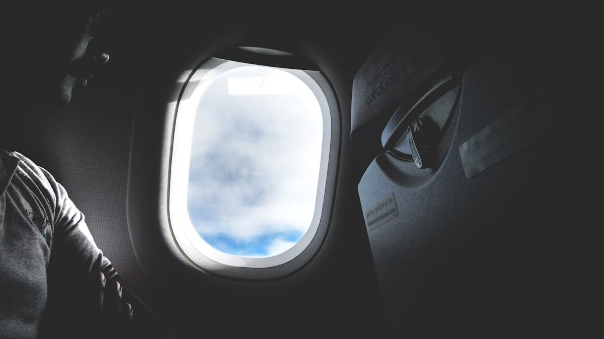 Passenger looking through airplane window at sunset - travel English 旅行英文