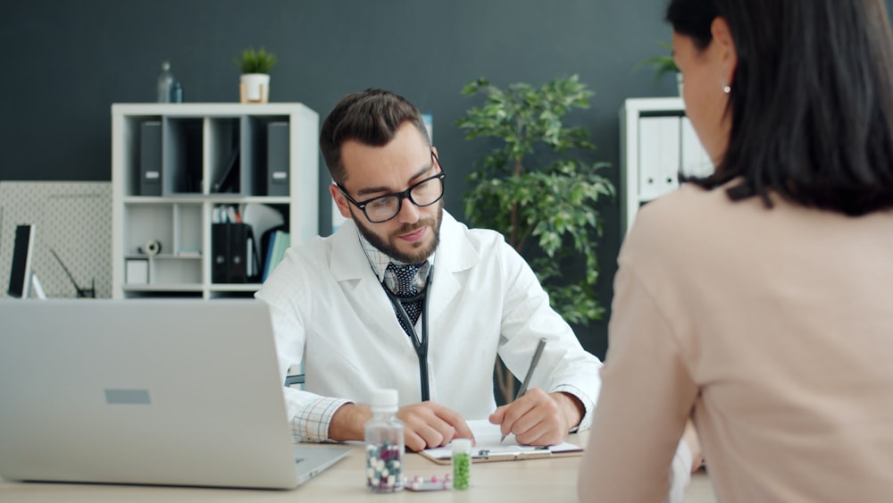Doctor writing medical notes while listening to patient describe symptoms in English