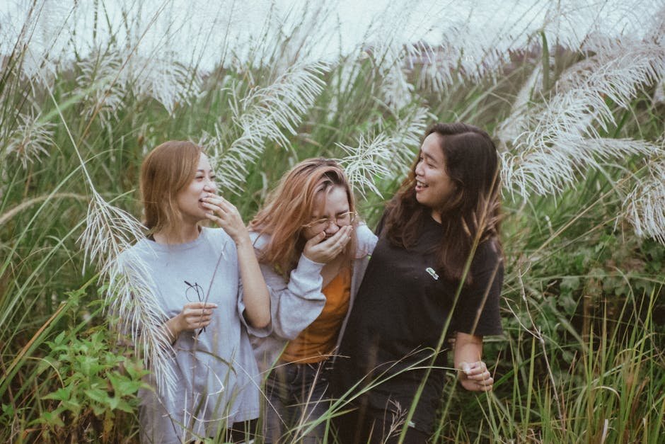 Three women enjoying a lighthearted moment amidst tall pampas grass in a natural outdoor setting. — body parts English idiom