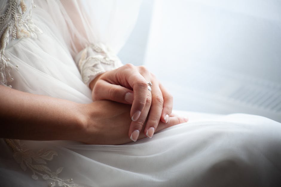 Close-up of a bride's hands in a delicate white gown, showcasing a wedding ring. — body parts English idiom