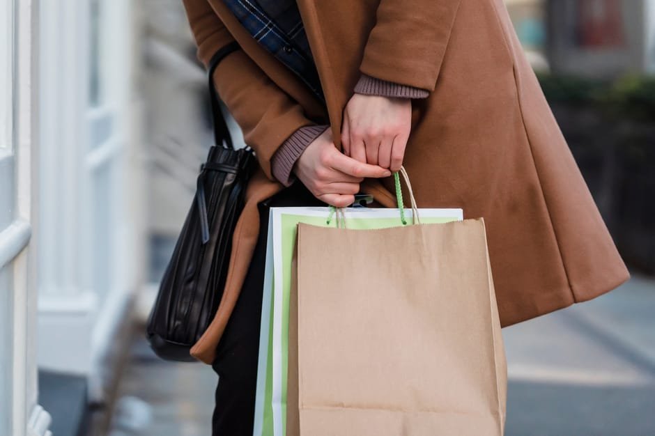 Crop unrecognizable female customer wearing coat standing with paper packets and handbag while shopping in city — body parts English idiom
