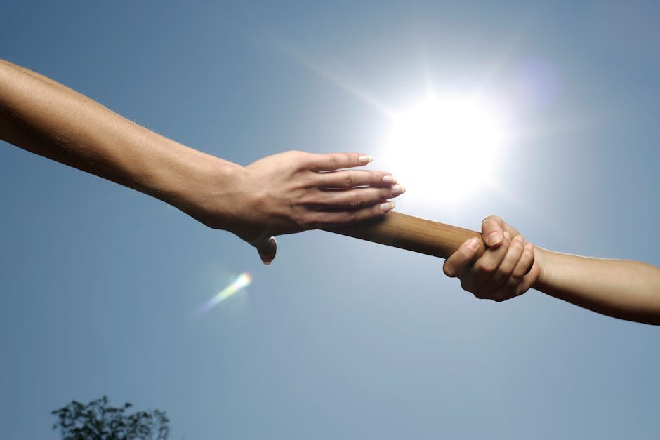Two hands passing a baton under a bright sun, symbolizing teamwork and cooperation. — body parts English idiom