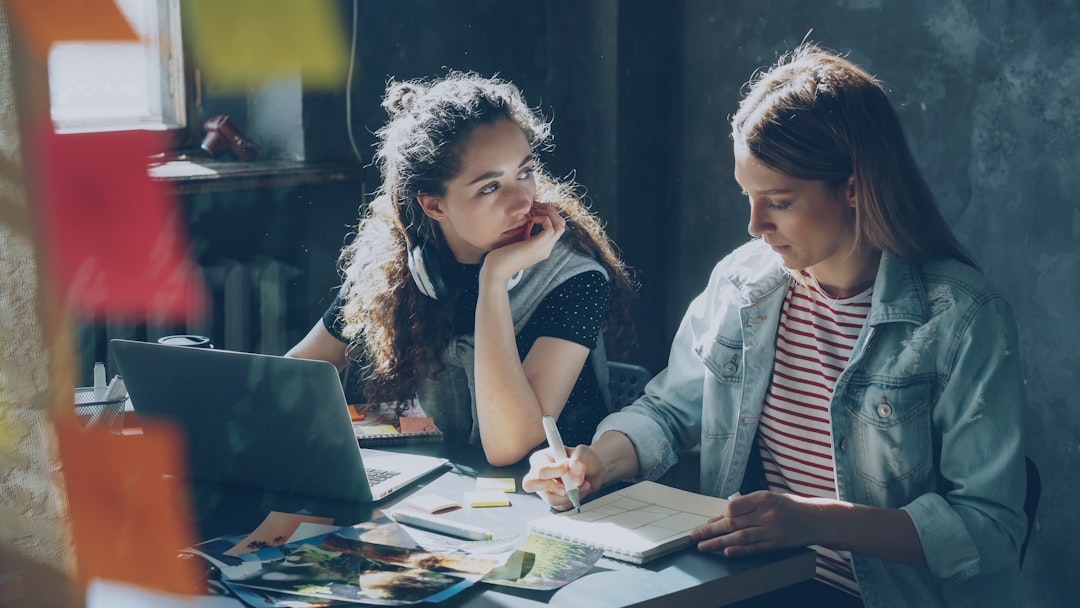 Cheerful pretty girl is working with laptop and listening to music, then taking off wireless headphones and talking with her 