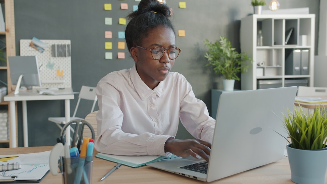 Tired mixed-race girl is using laptop computer and suffering from headache in creative office, lady is touching head and expr