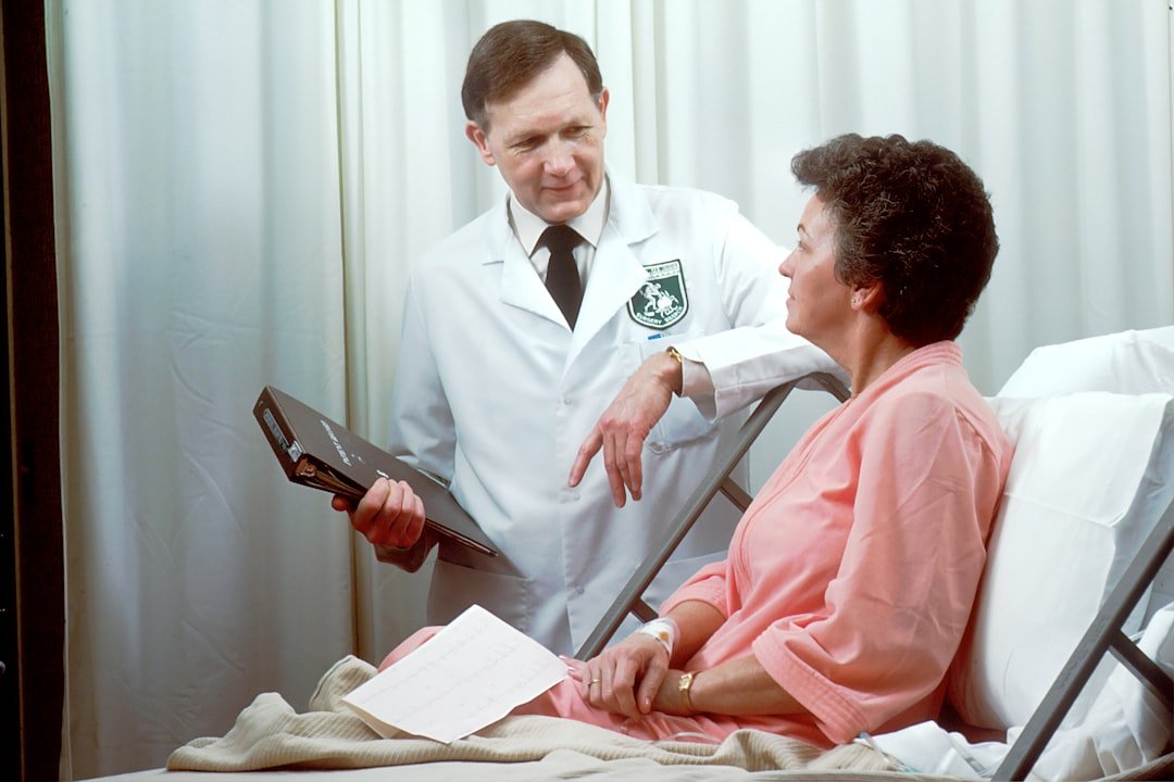 A Caucasian male doctor from the Oncology Branch consults with a Caucasian female adult patient, who is sitting up in a hospi