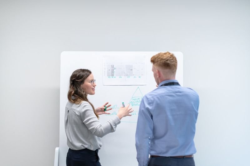 Two colleagues at whiteboard wrapping up with 簡報英文 closing phrases