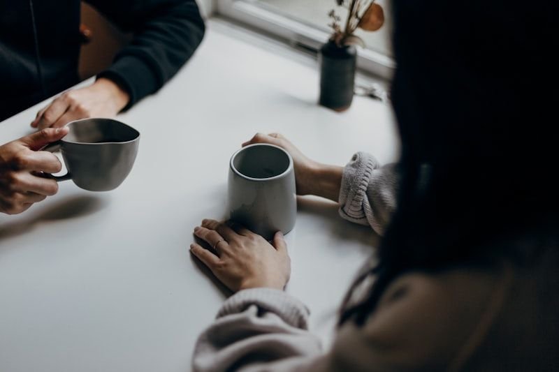 兩人隔著桌子端著咖啡杯交談，象徵人際關係的英文諺語