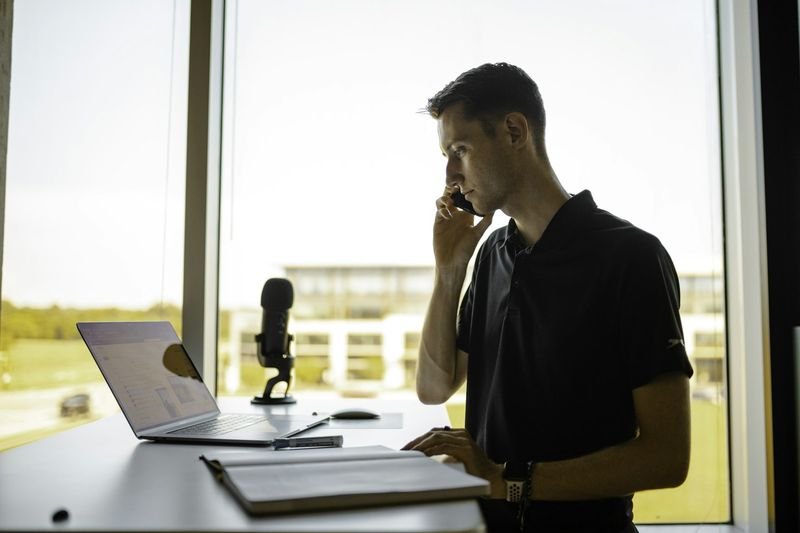 Man answering the phone in English at a standing desk with a laptop
