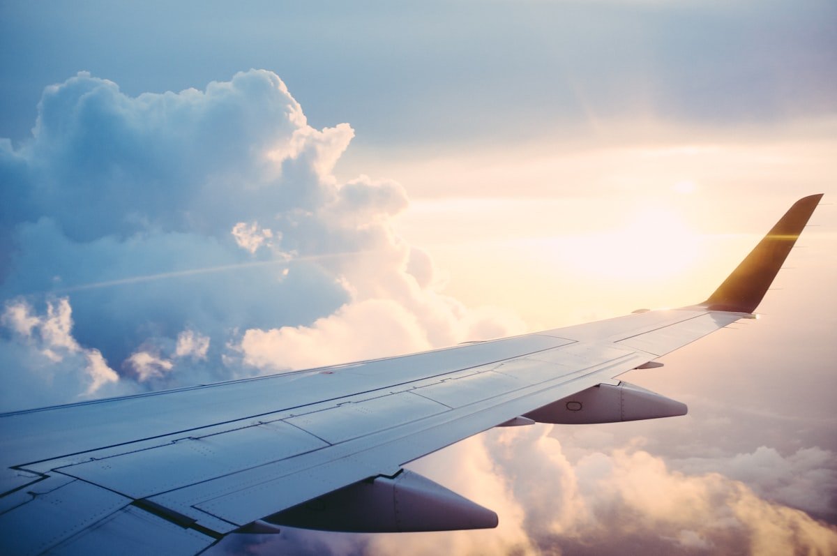 Airplane wing cutting through soft pink and blue clouds at sunset during a flight