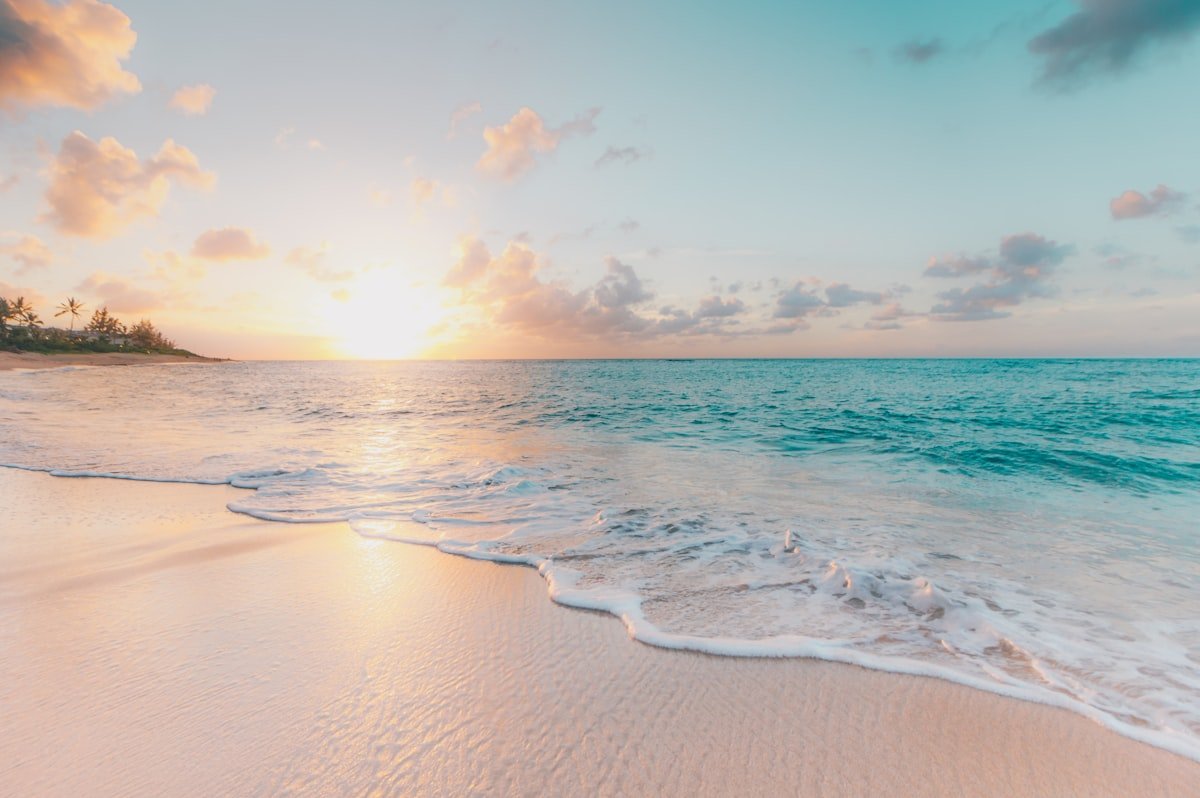 Calm turquoise waves rolling onto a golden sunset beach, the perfect change of scenery
