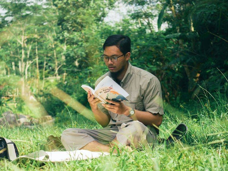 Man reading an English book outdoors in a park on the weekend