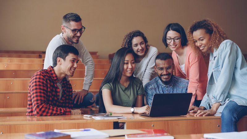Diverse students learning English together with a native speaker around a laptop