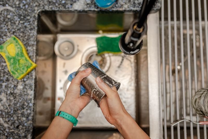 Person washing dishes at a sink showing the do vs make collocation do the dishes