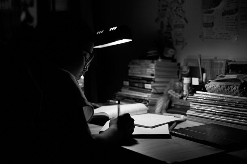 Burn the midnight oil idiom — desk lamp glowing in dark room during late night study