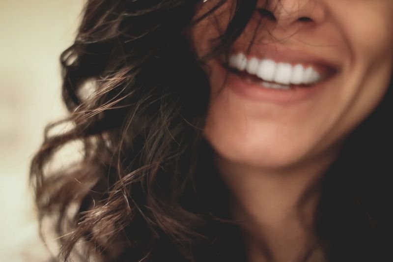 Describe hair and face in English - woman with dark curly hair smiling