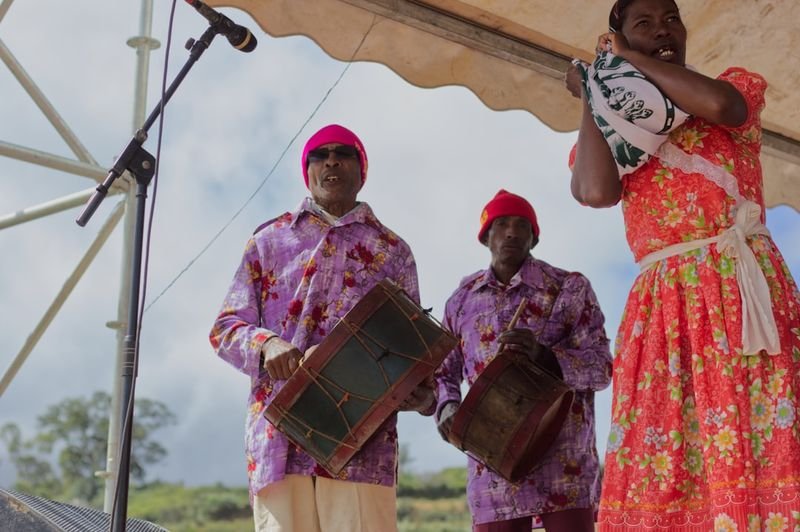 Three musicians in colorful traditional costumes playing heritage drums in a cultural music performance