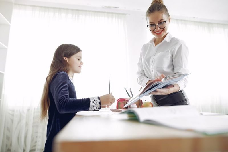Teacher helping student with homework — turn in meaning to submit work (turn in 繳交 片語)